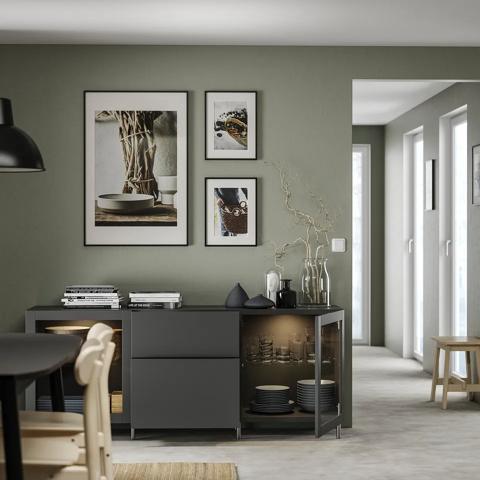 A sage green dining area with a black BESTÅ sideboard, art, table & chairs.