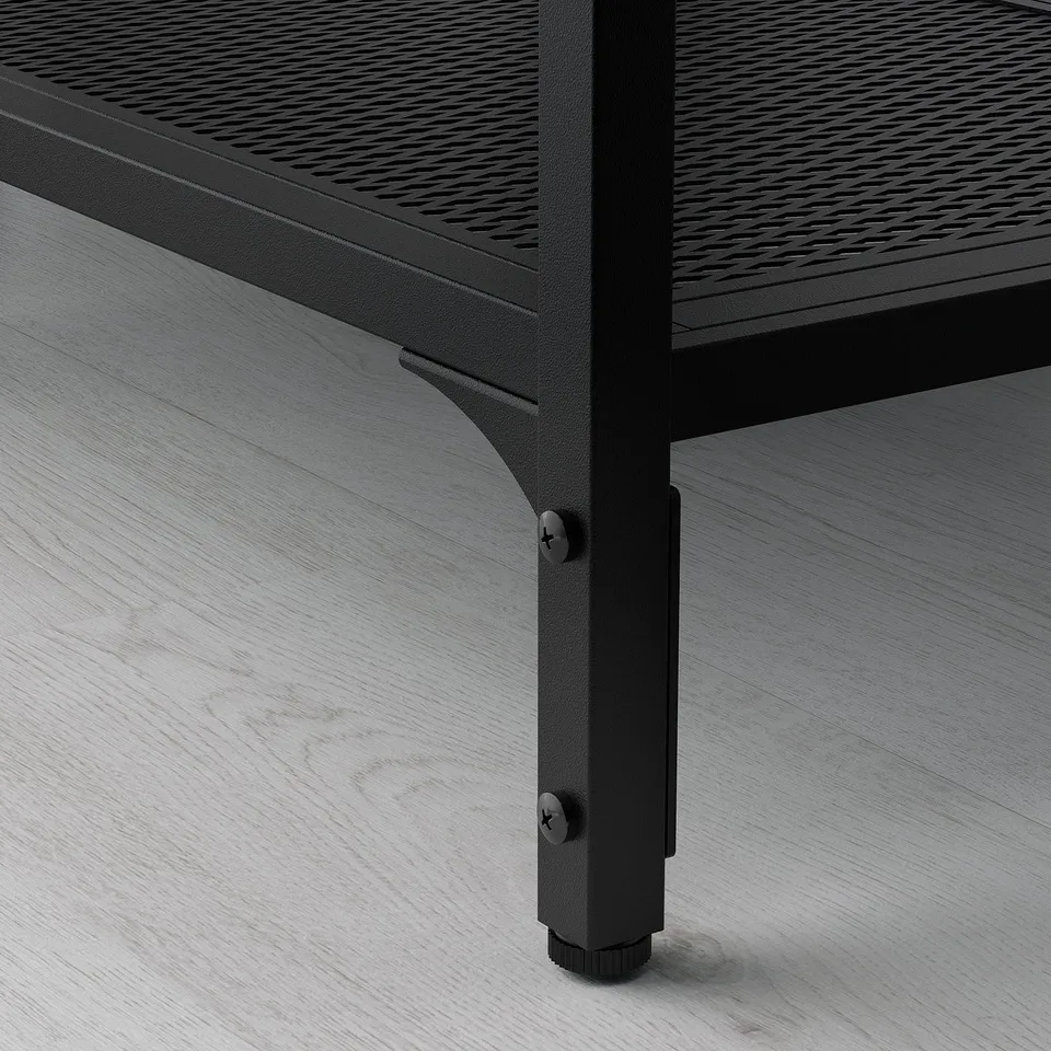 Black metal tv stand with adjustable feet on wooden floor.