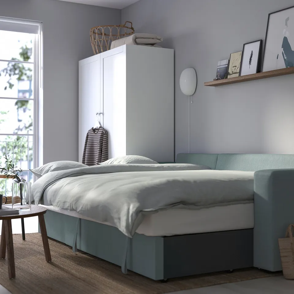 Cosy bedroom with green BÅRSLÖV sofa-bed, white linens, wooden side table, large window.