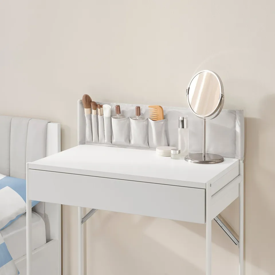 White dressing table with a drawer and fabric pockets. Store makeup, brushes, and accessories neatly. Mirror stands on the table.