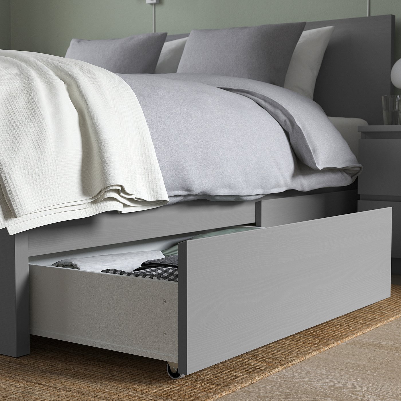 Bed with open storage drawer under frame holds folded clothes, grey bedding.