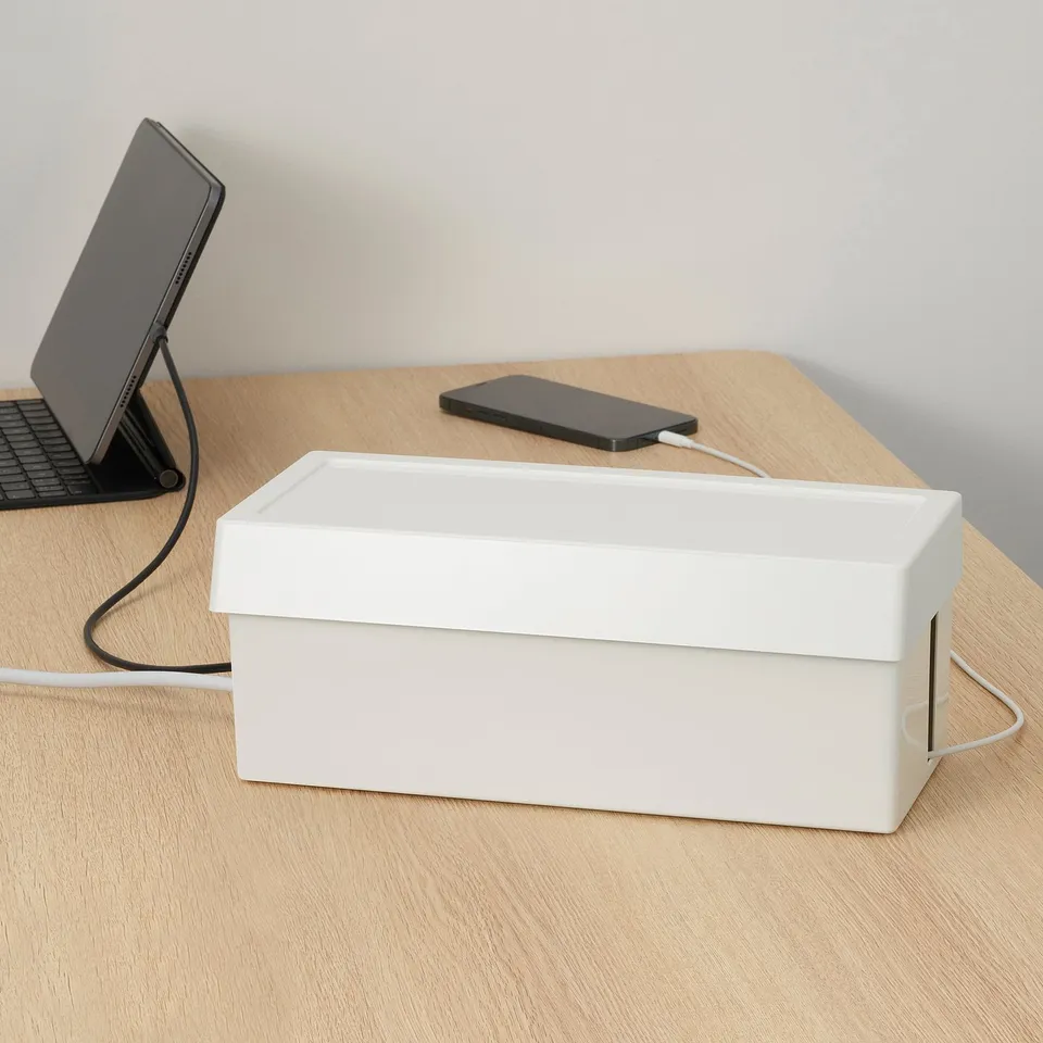 Small white SÄTTING box on desk, stores and tidies cables. Next to propped tablet, phone.