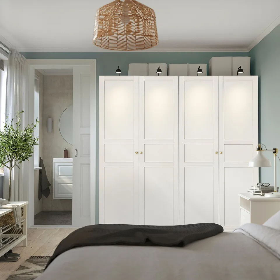 Modern minimalist bedroom with large white PAX wardrobe, black bed, and wicker hanging lamp.