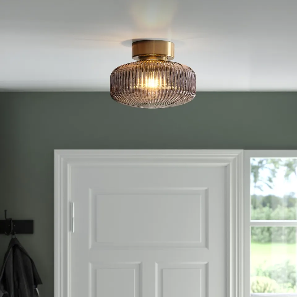 A modern, flush-mounted light fixture with a brass base and clear glass shade, providing warm, ambient light.