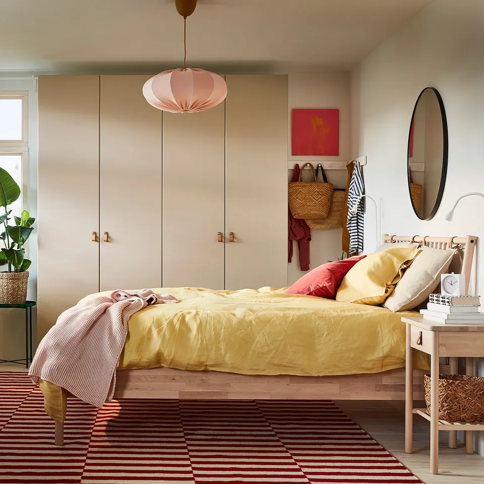 Wooden BJÖRKSNÄS bed with yellow linens, pink accents, and colourful décor.