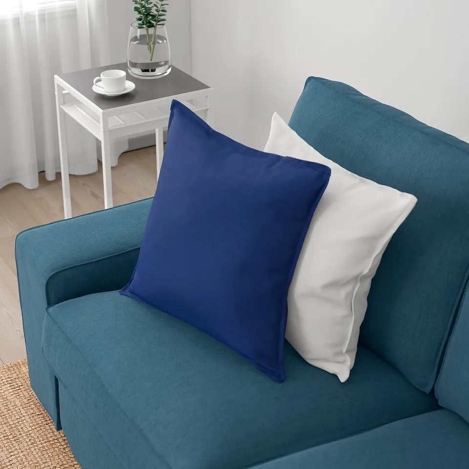 Blue sofa with two pillows, one white, near white side table with cups and plant.