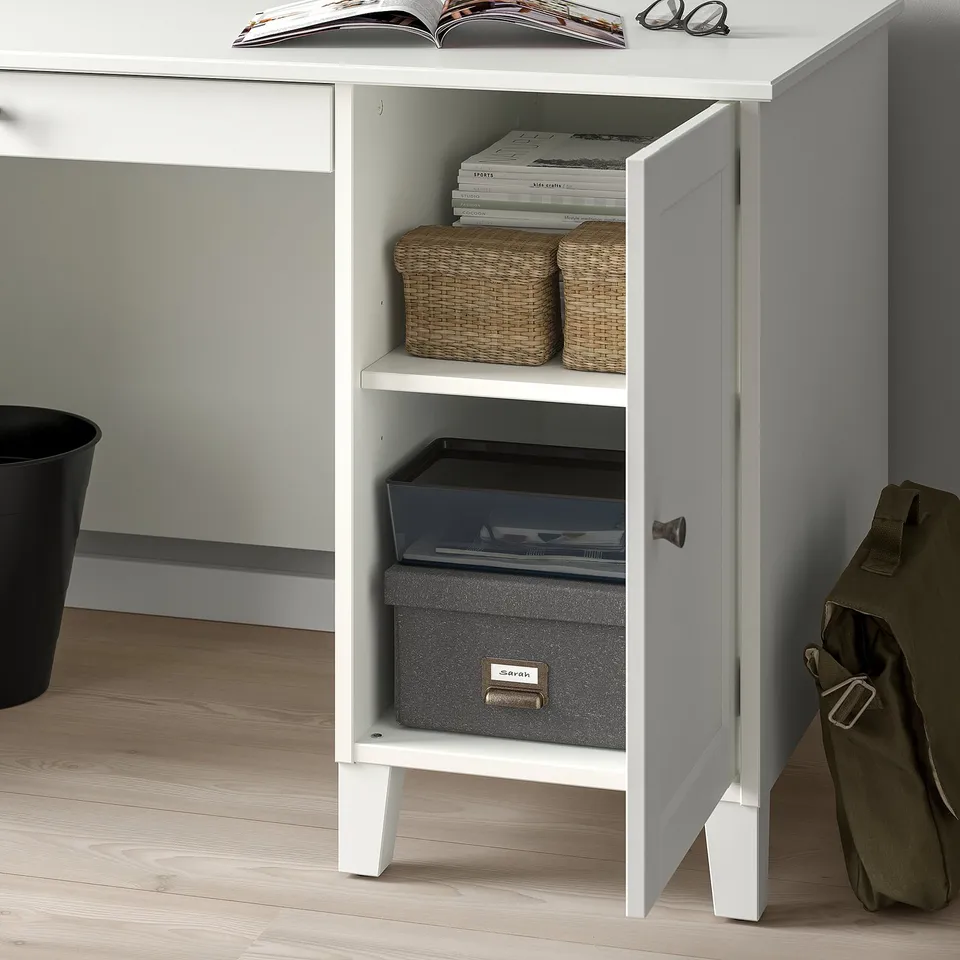 White desk with open door revealing woven baskets and boxes for organised storage.