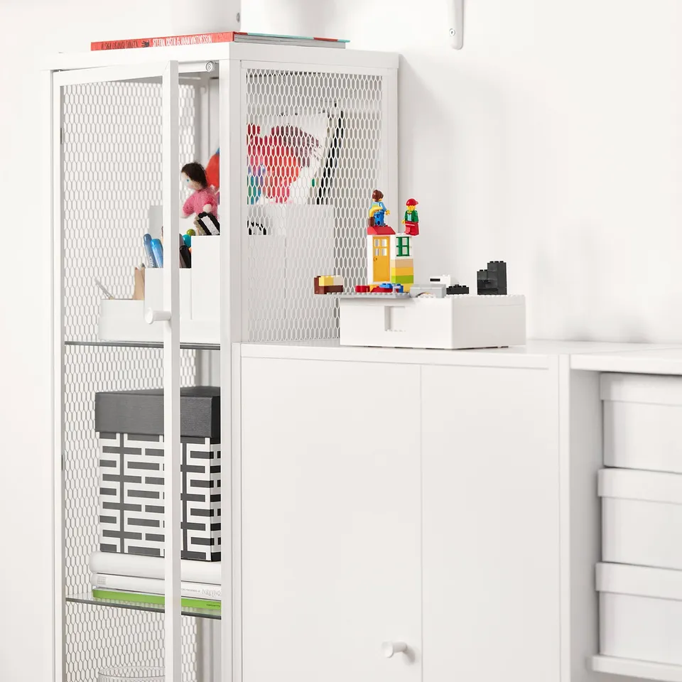 White BAGGEBO storage unit with mesh and glass doors, organising toys and books, sleek modern design.