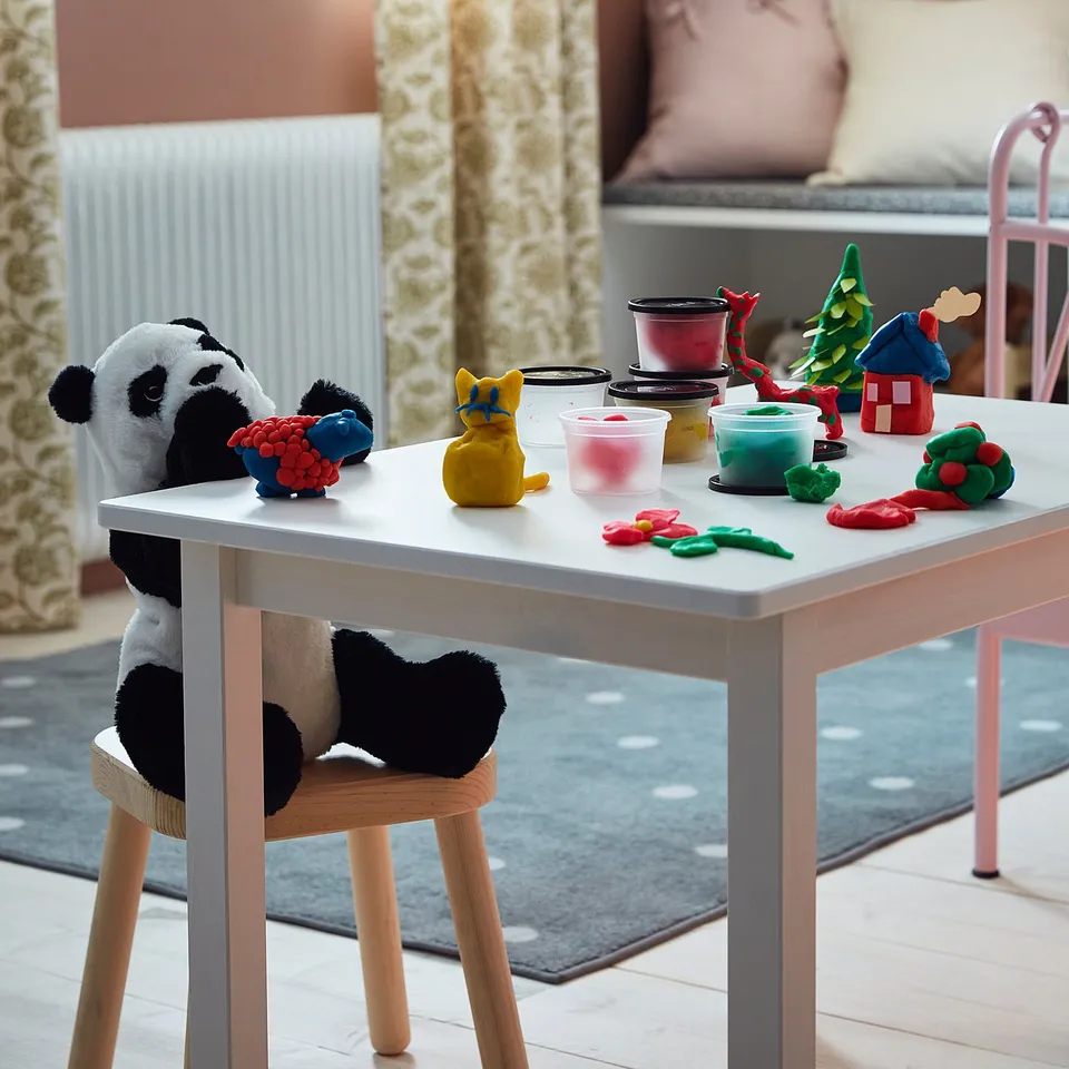 Childrens craft table with MÅLA modelling dough in various colours, a panda chair, and a rug in a cosy room.