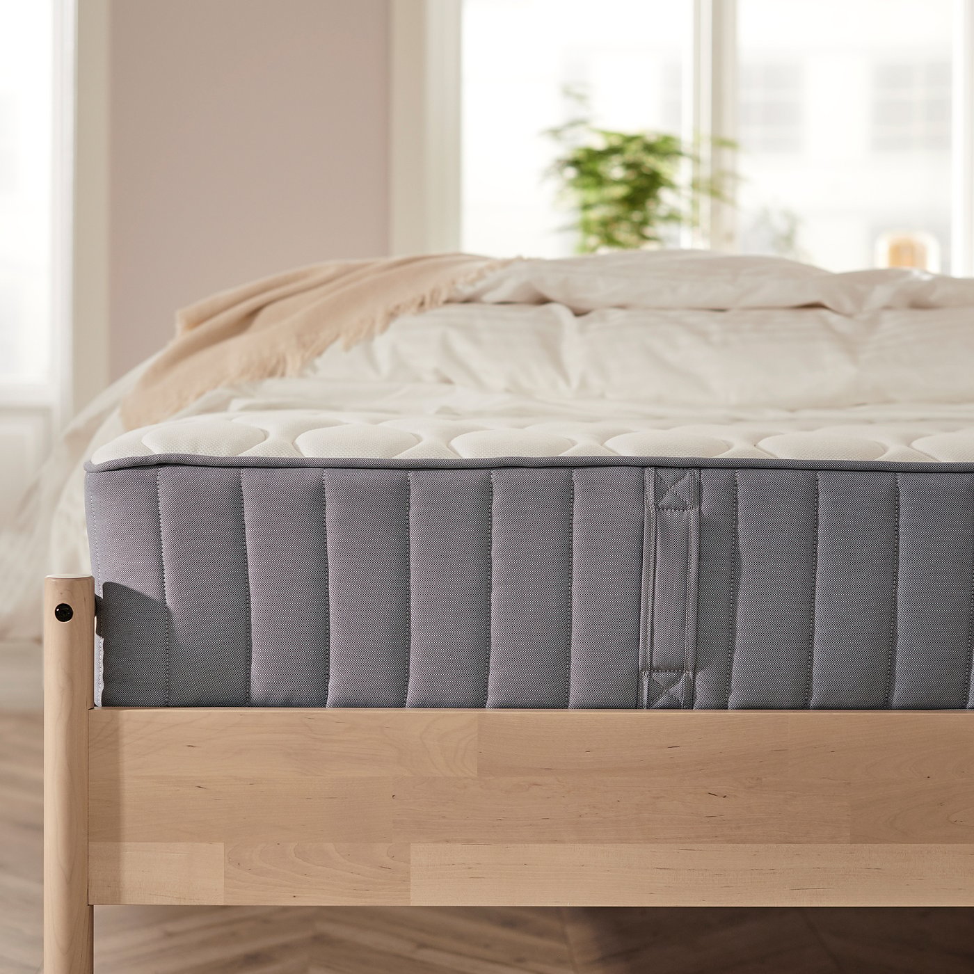 Modern bed with VÅGSTRANDA mattress, beige linen, wooden frame, natural light.