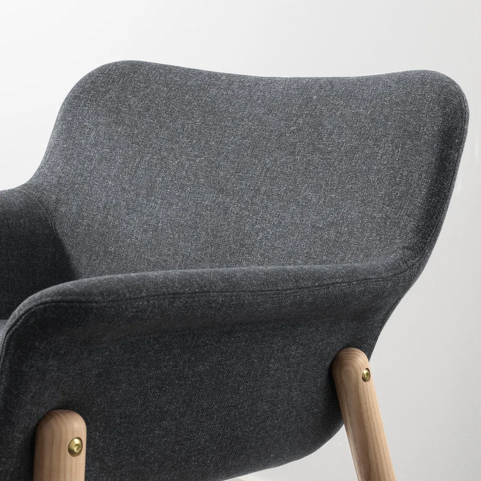 Dark grey upholstered chair with wooden legs. Soft, curved lines. High-quality fabric and sturdy wooden frame.