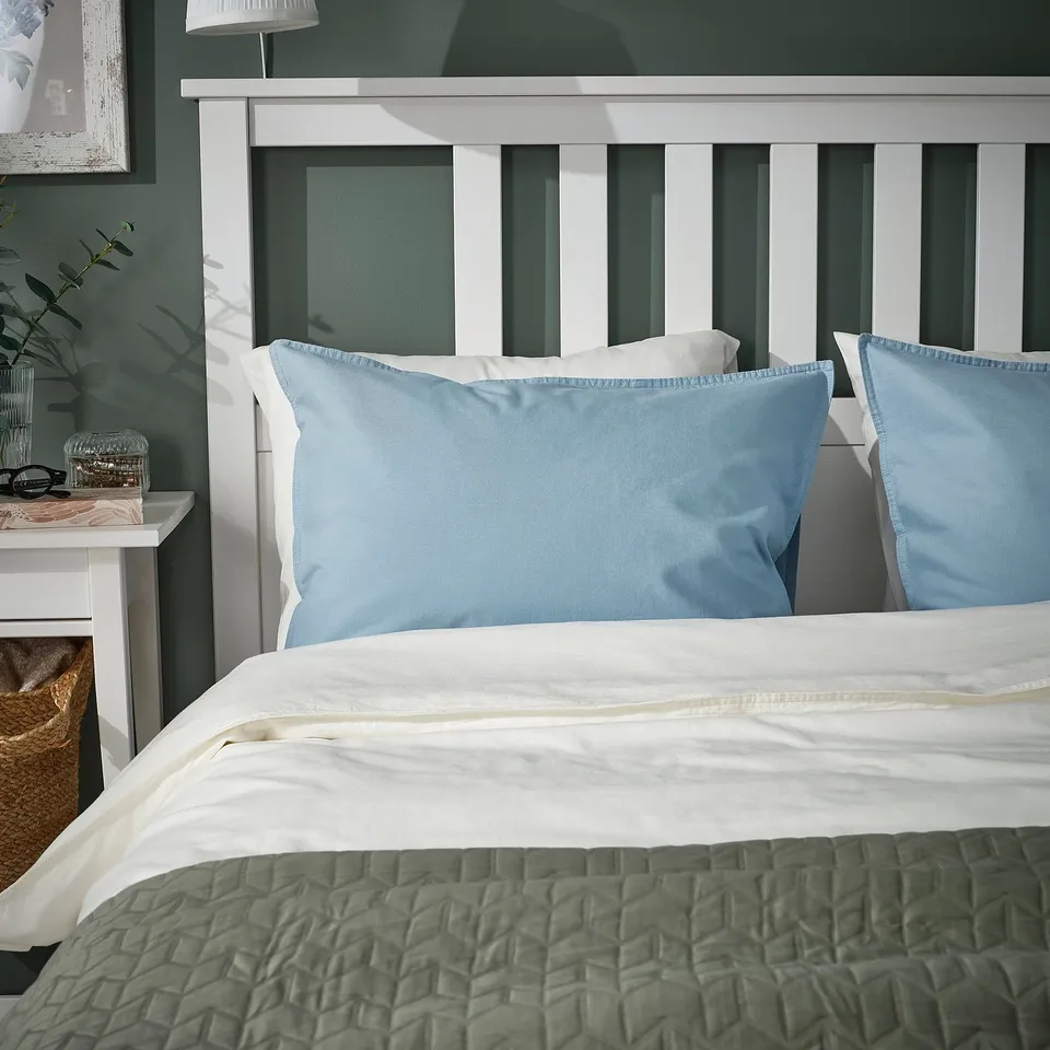 Blue ÄNGSLILJA pillowcase on bed with white headboard and green blanket.