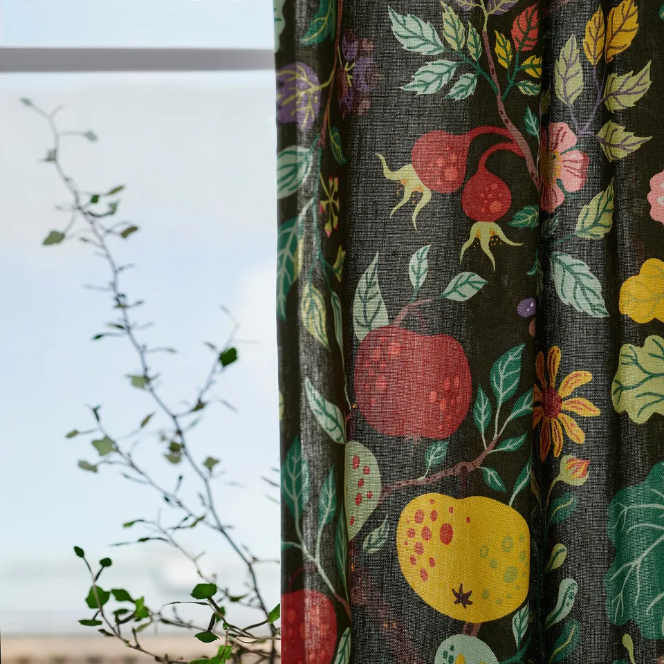 Dark green curtains with colourful floral prints partially cover a window, allowing soft light and a view of bare branches outside.