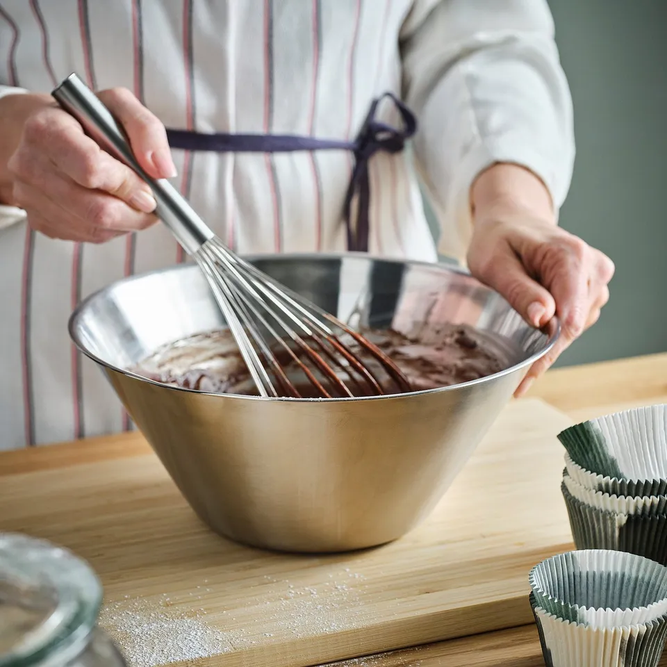 Person whisking chocolate mixture in large stainless steel bowl on wooden board.