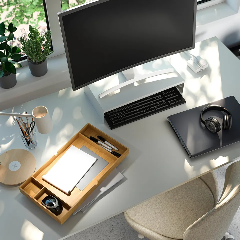 Desk with monitor, keyboard, laptop, headphones, and stationery; organised with wooden tray.