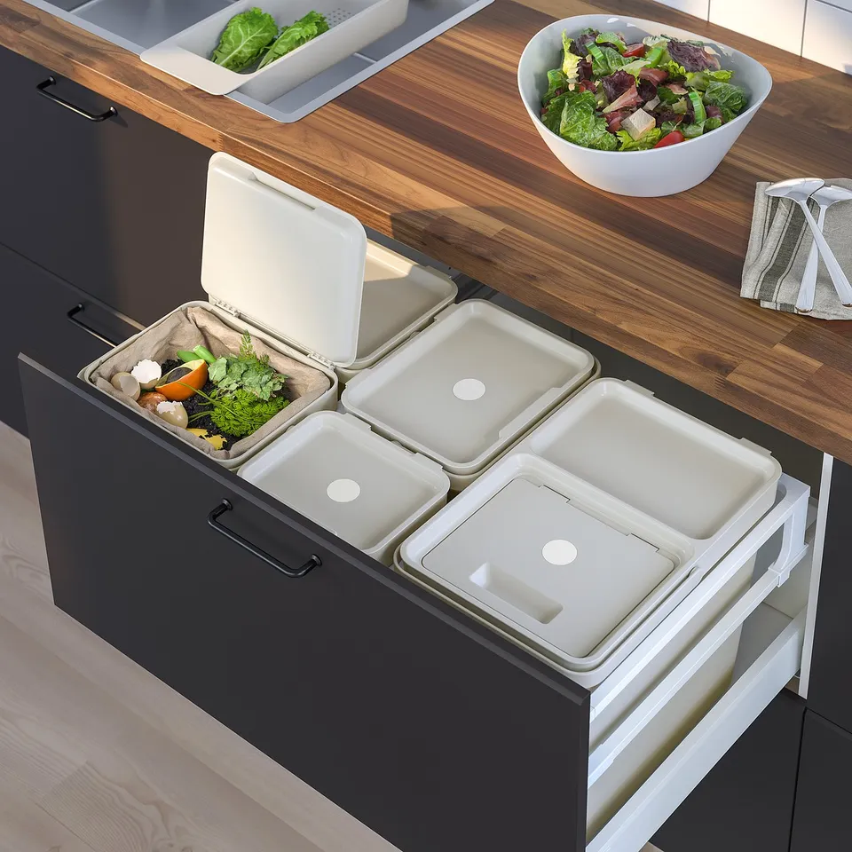 Modern kitchen with integrated waste sorting. Four HÅLLBAR bins in drawer, organic waste visible, wooden countertop with salad bowl.
