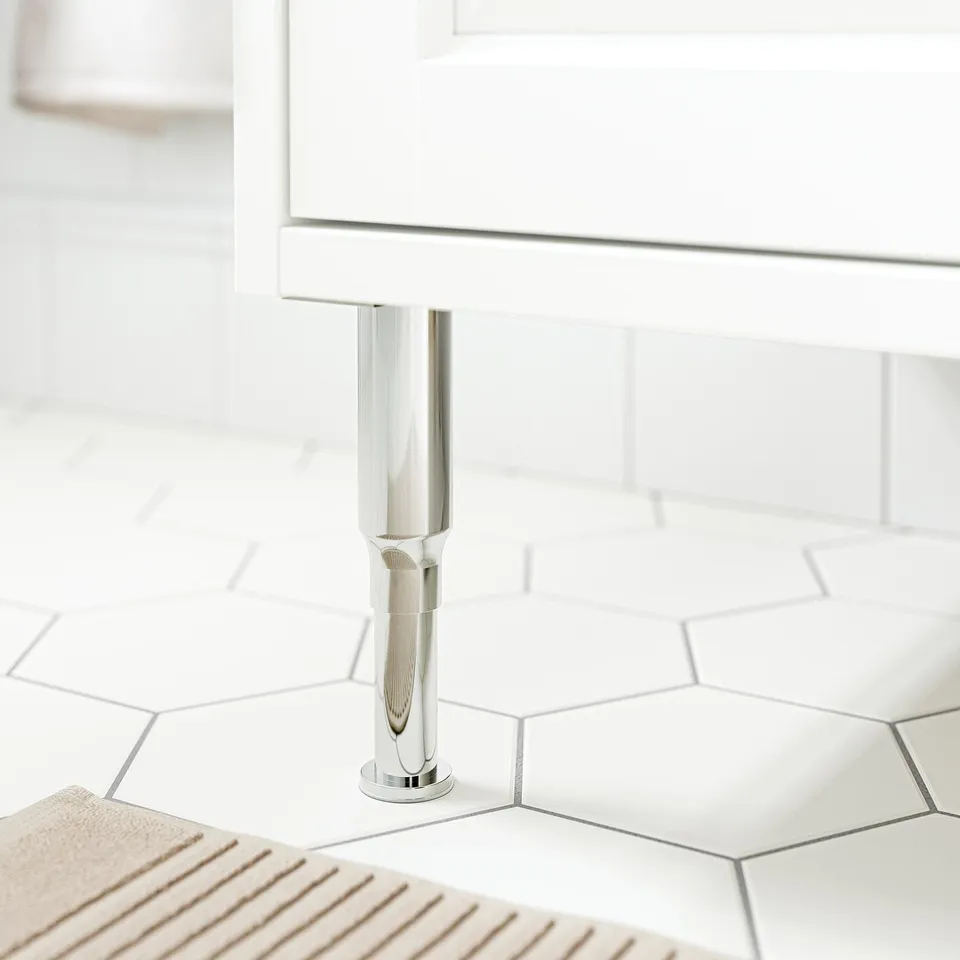 Modern bathroom cabinet leg in stainless steel, sleek and polished for durability, supporting white cabinet on reflective hexagon tiles.
