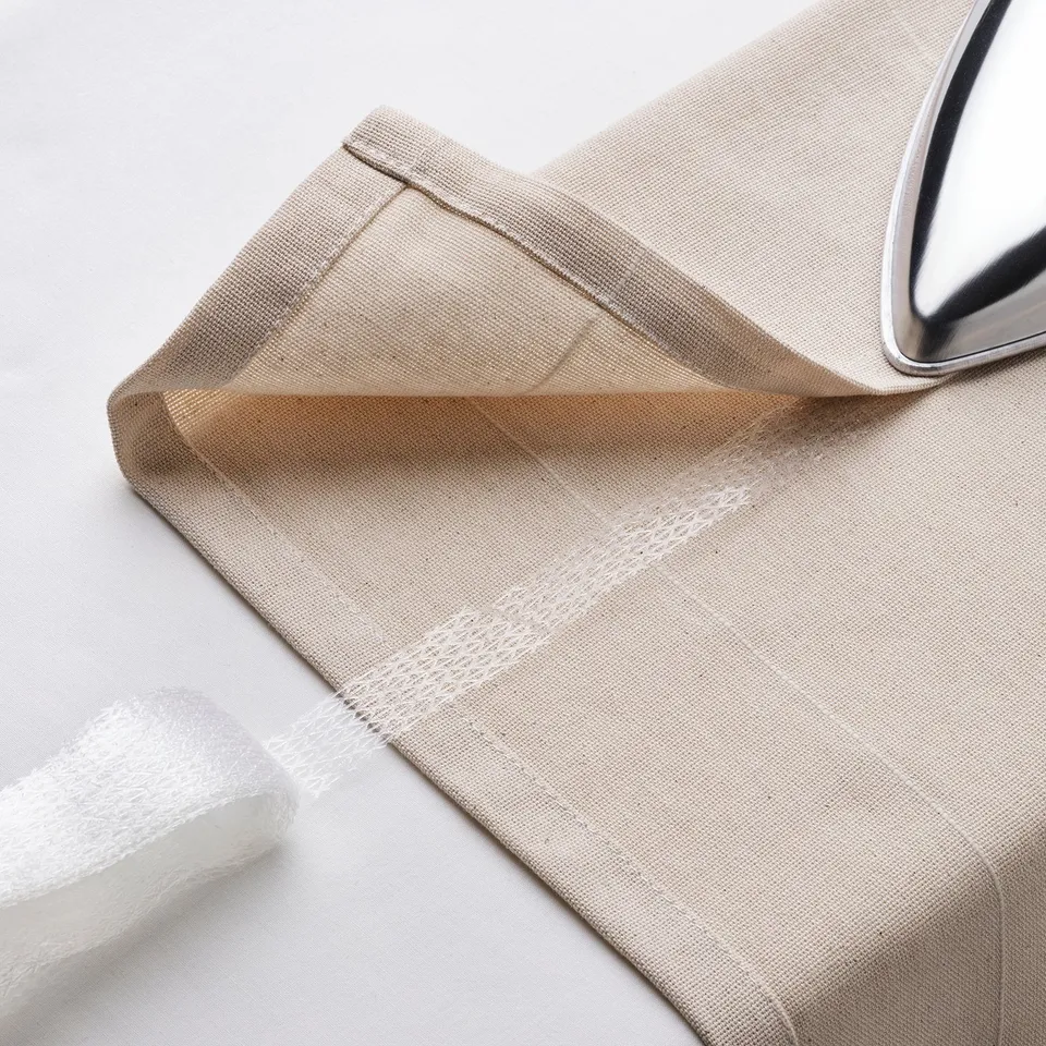 Close-up of off-white curtain with header tape and metal hook.