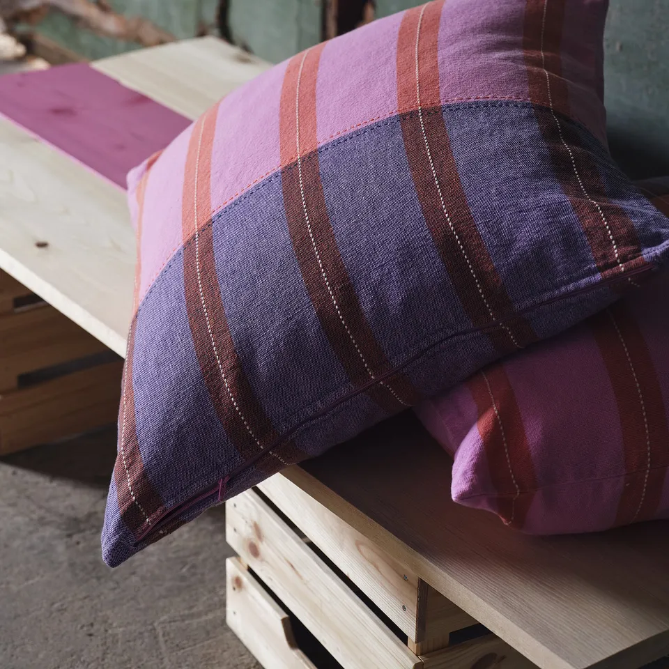 Colourful striped pillows on wood bench, one side embroidered.