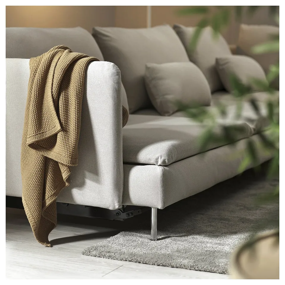 Modern grey sofa-bed with cushions and blanket, on a rug, in a cosy room.