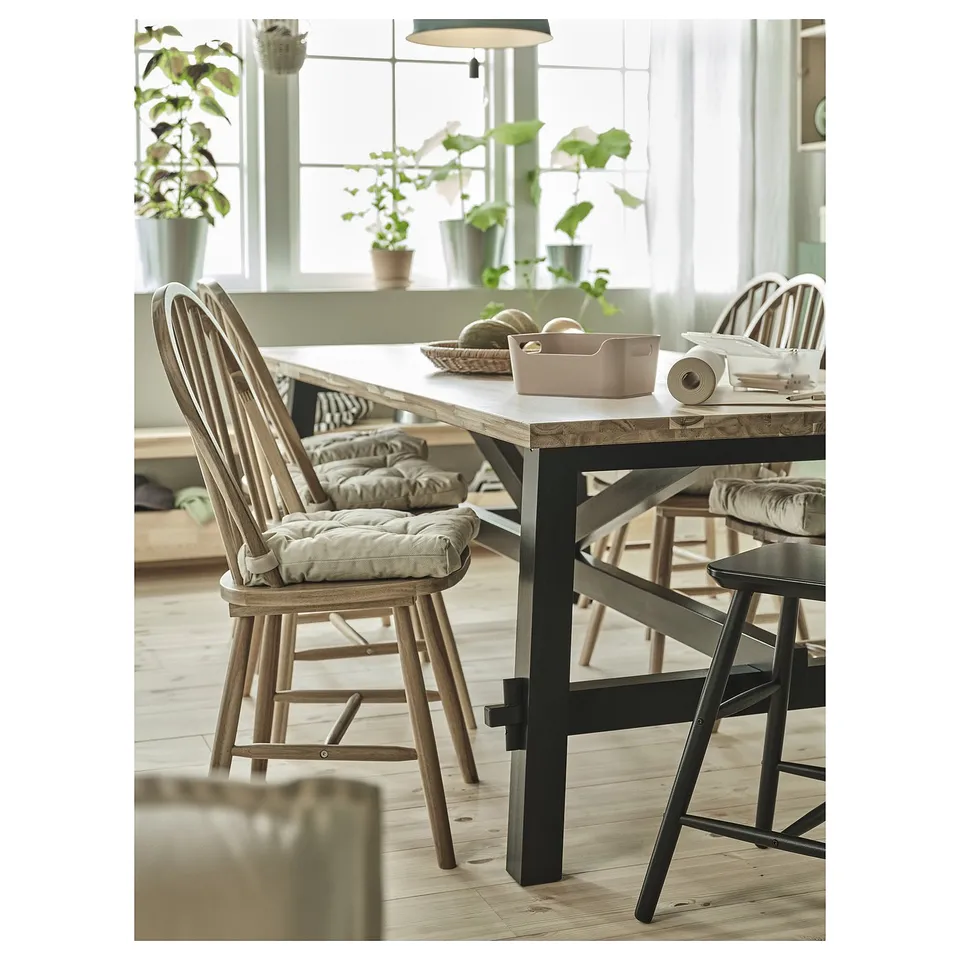 Bright dining area with large window, wooden table, MALINDA beige chair pads, potted plants, and black metal chairs.