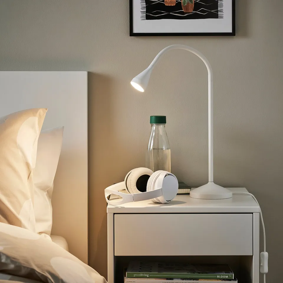 NÄVLINGE lamp on bedside table with water bottle, headphones, bed & pillows, picture.