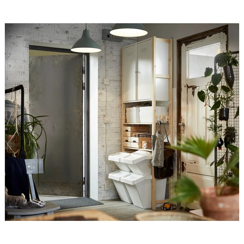 A room with IVAR storage unit made of light wood and white bins. Plants, a door, and a mirror are also visible.