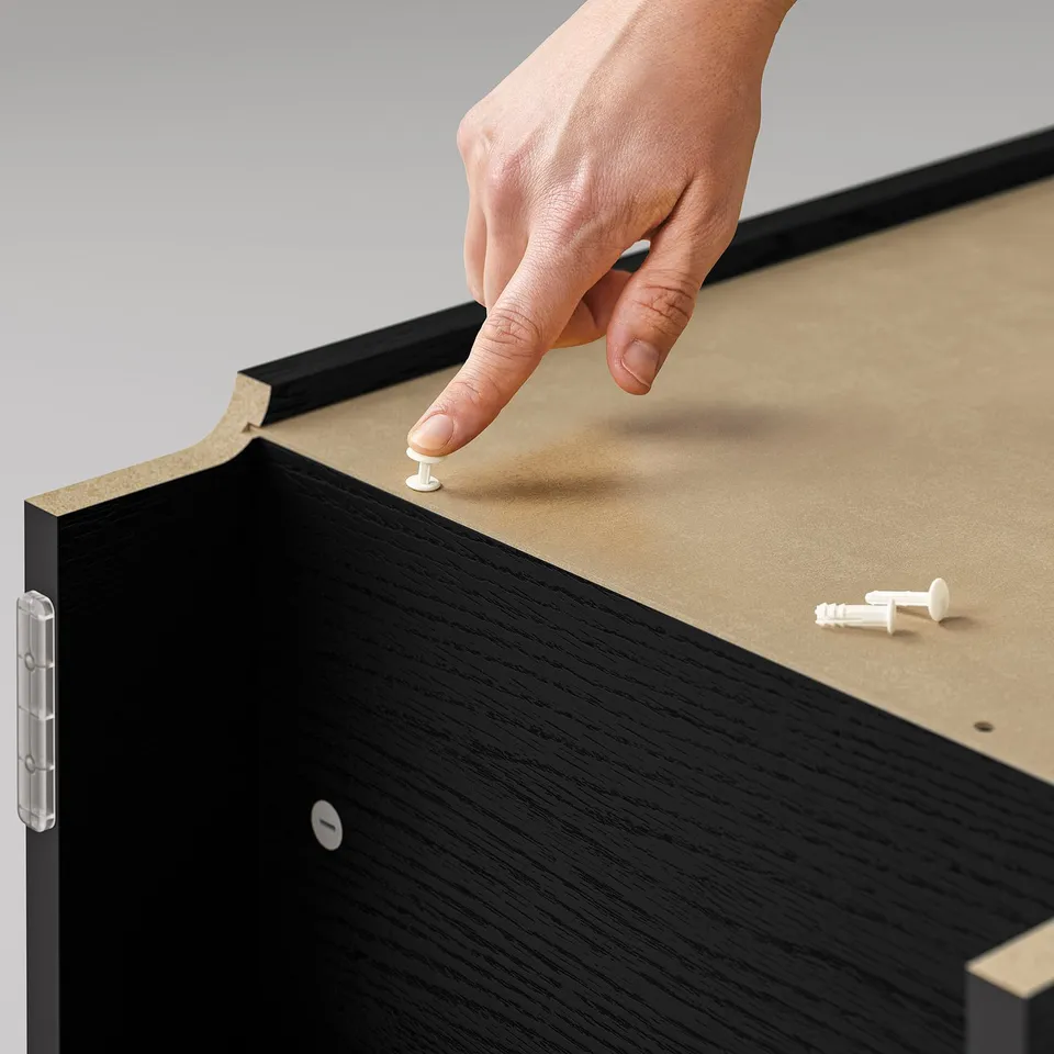 A hand assembles a black BILLY bookcase, using white screws on a grey background.