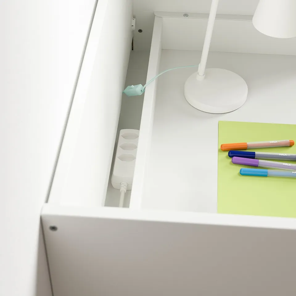 A clean, white desk setup featuring a modern lamp and colourful pens, with a drawer stopped to prevent tipping.