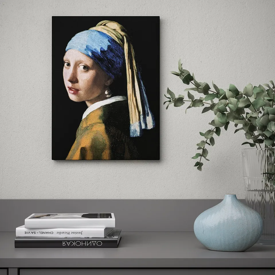A framed painting of girl with a pearl earring by jan vermeer hangs on a wall above a shelf with books and vases.