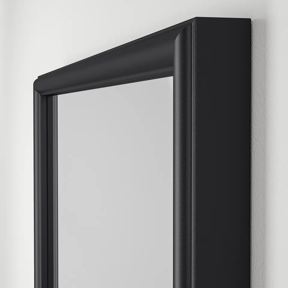 Black-framed decorative mirror, reflecting light, mounted on a simple wall.