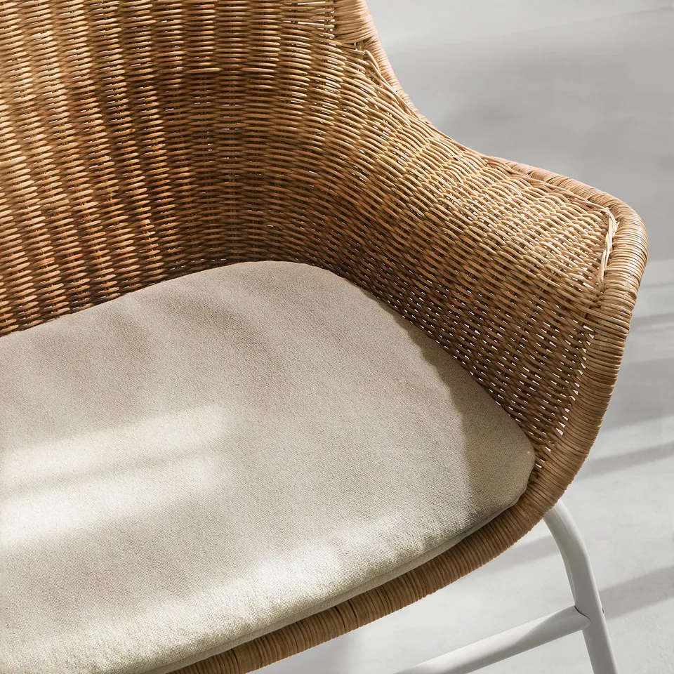 A wicker chair with a beige cushion, intricately woven, providing a cosy and stylish seating option.