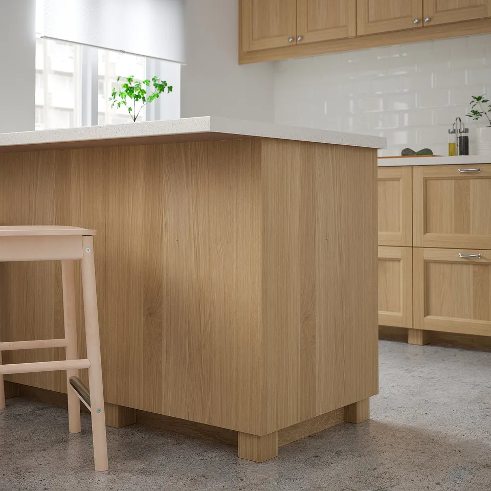 VEDHAMN kitchen island in natural wood, solid oak legs, with beige countertop, smaller than surrounding cabinets.