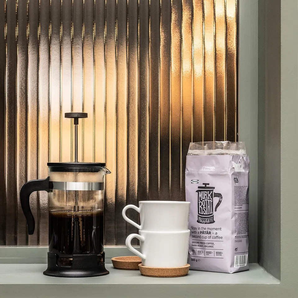 Black cafetière coffee maker with white cups and coffee bag on window sill.