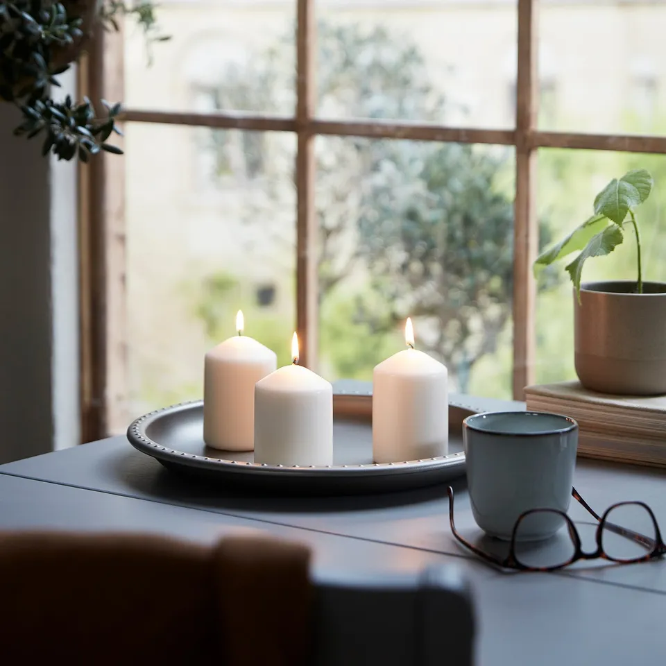 Three lit candles on a tray by window, creating warmth and ambiance.