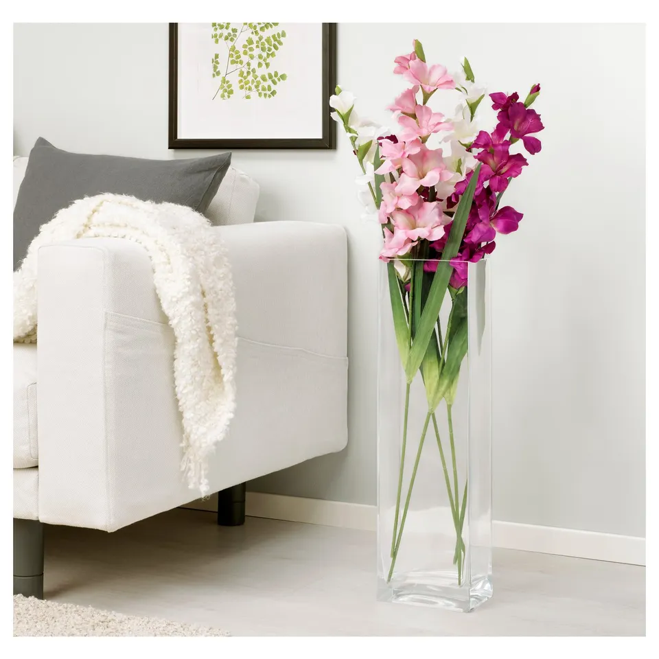 Clear acrylic vase with pink and purple artificial flowers next to a white chair with a blanket.