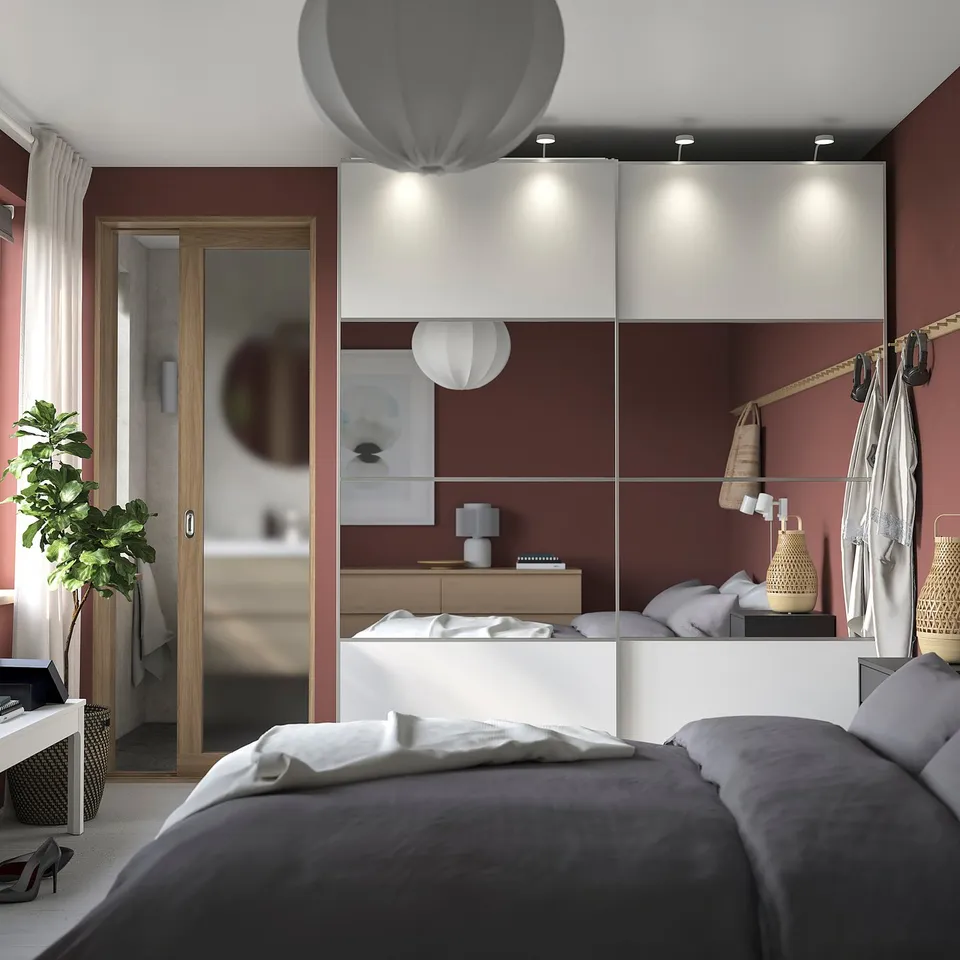 Modern bedroom with grey bed, red walls, white cabinets, hanging lamps, plant, and slippers.
