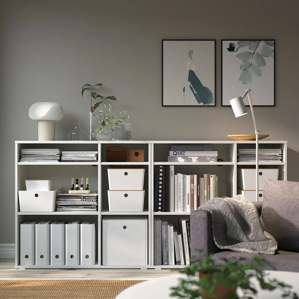 Modern living room with KUGGIS storage, books, plants, art, and blanket on sofa.