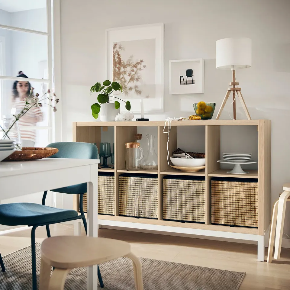 Modern living room with wooden KALLAX shelf, blue chairs, plants, and decorative items.