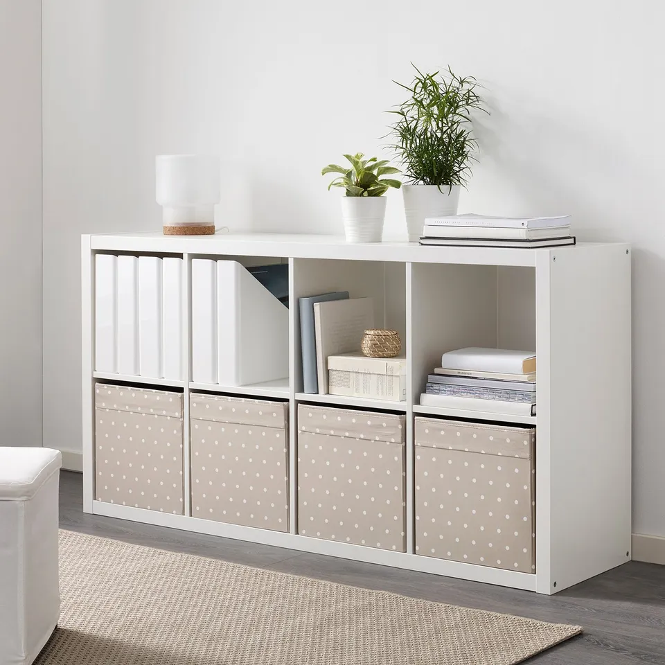 White kallax unit with fabric boxes, holding books, baskets, and plants.