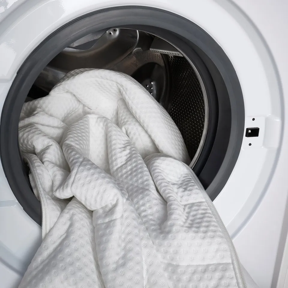 White washing machine with open door, loading a large white comforter.
