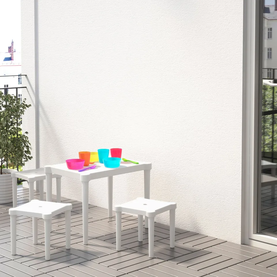 Bright kids play area with white UTTER table and chairs, colourful cups, and spoons on a balcony, perfect for outdoor fun.