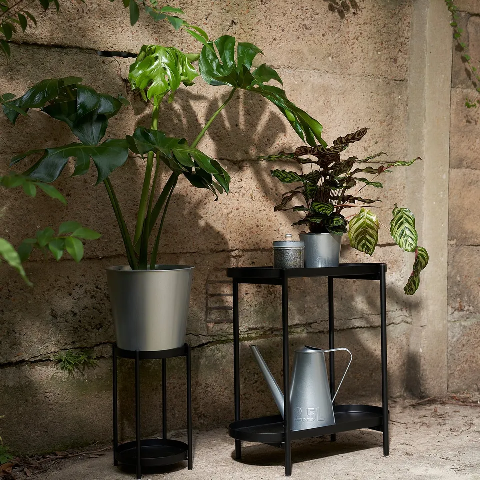 An image showcasing ÅKERBÄR watering can, grey, made of rust-resistant steel, stored on a shelf, smaller than the pots