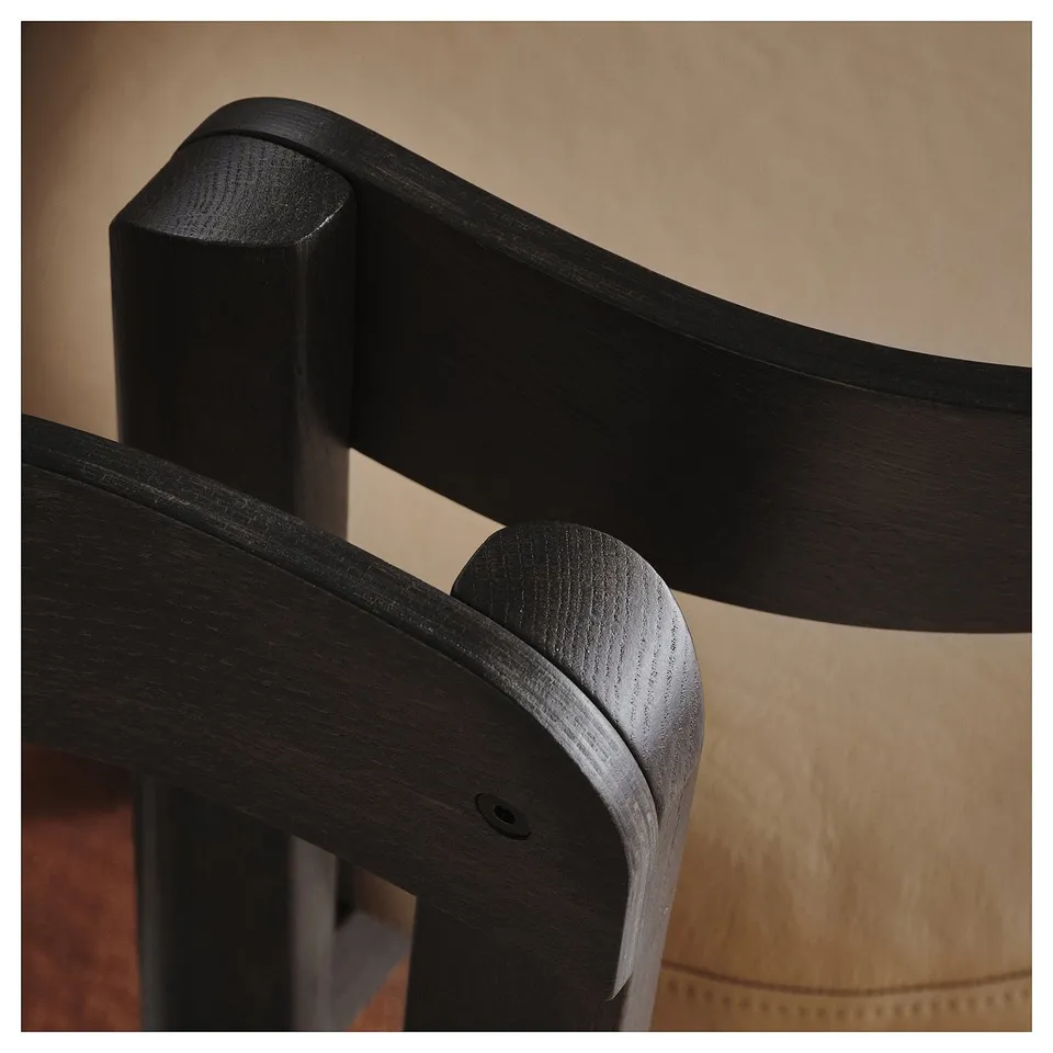 Dark wooden chair back with smooth finish and curved armrest, set against a neutral background. High-quality craftsmanship evident in sleek design.