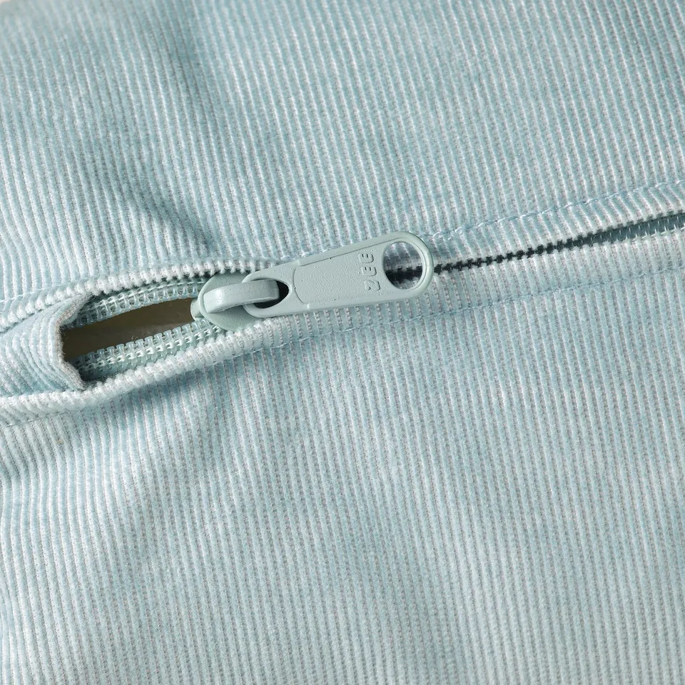 Zip on light blue corduroy fabric, zip partially open, close-up shot.