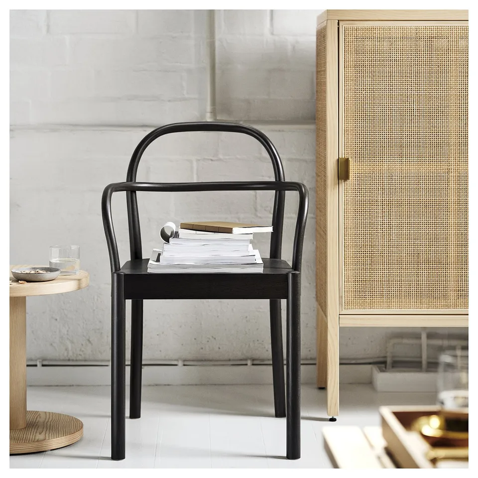Modern black STOCKHOLM 2025 chair with curved back, holding books in front of cabinet.
