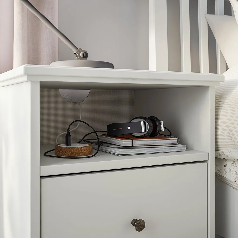 White modern two-tier shelf unit. Top shelf has a grey lamp, bottom holds black headphones and books.