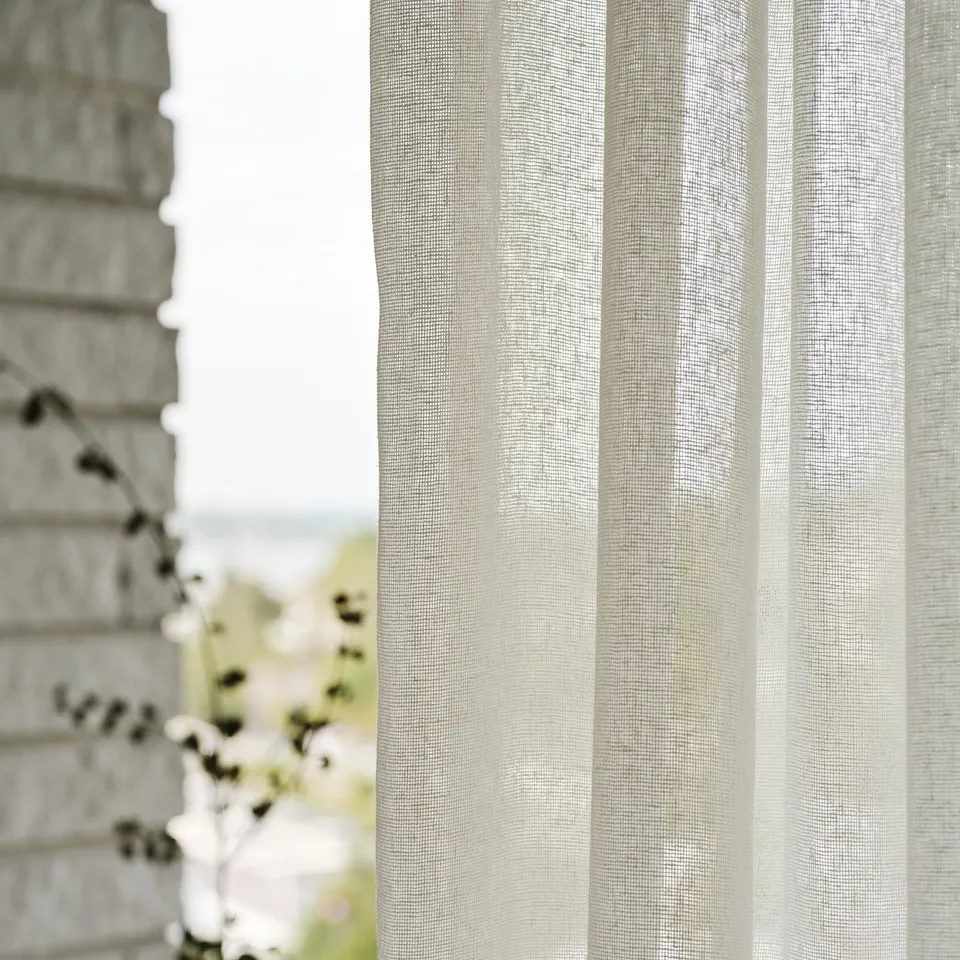 Sheer curtains with striped texture hang by window. Light philtres through fabric, creating soft glow.