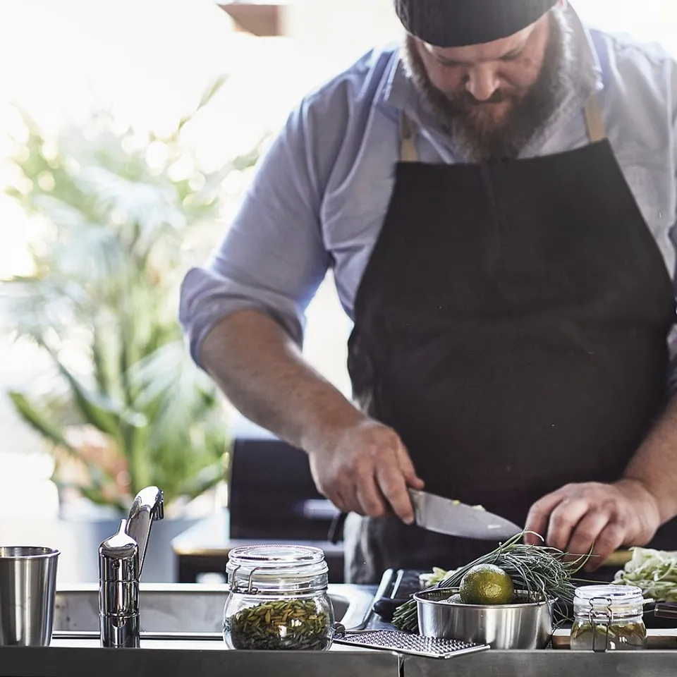 Person with beard grills outdoors, using various fresh ingredients.