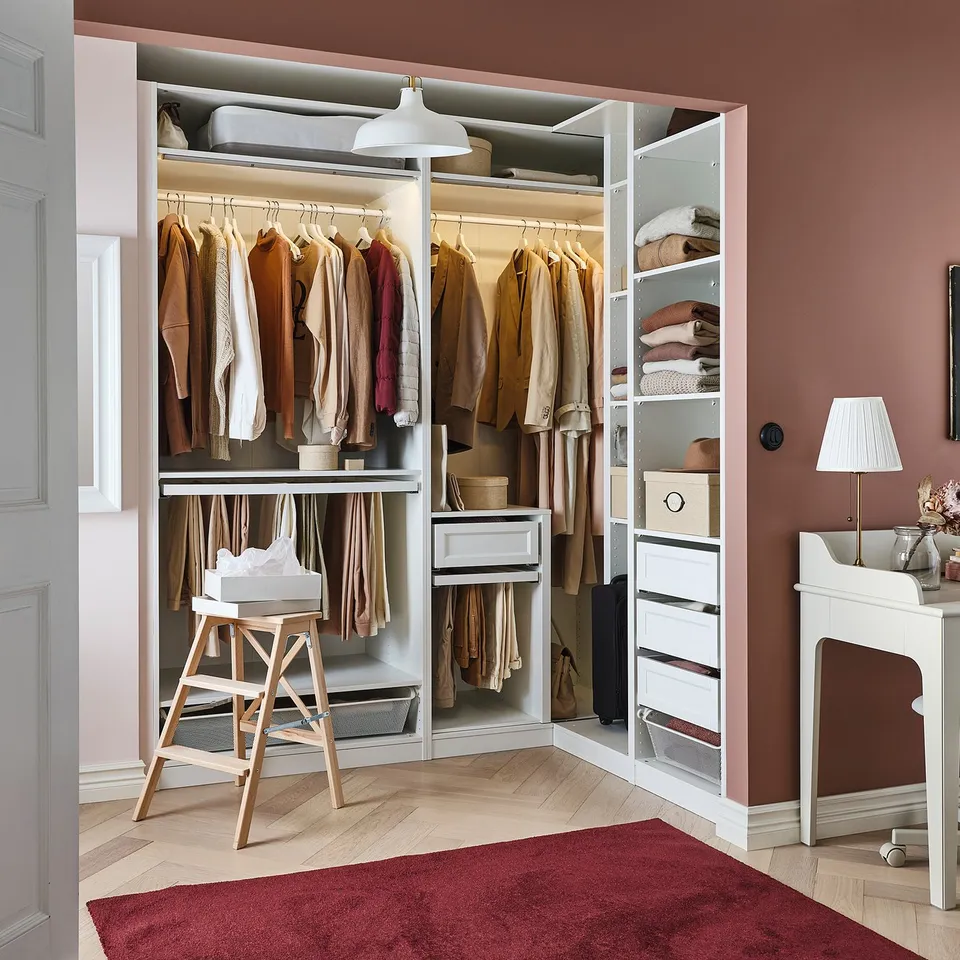 Organised IKEA PAX closet with clothes, shelves, drawers, stool, and red rug.